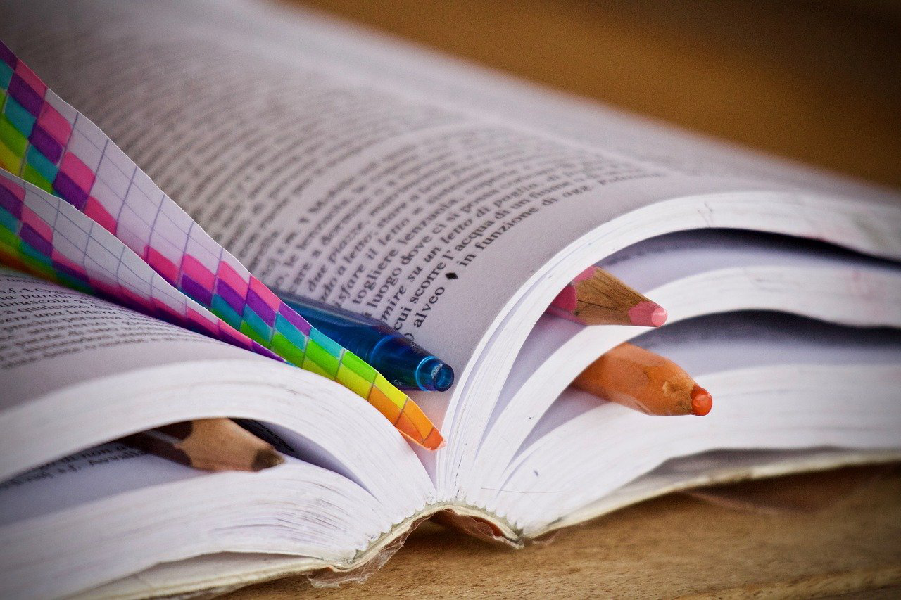 aufgeschlagenes Buch mit Buntstiften und Notizzetteln
